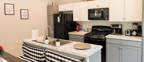 A modern kitchen with a central island, black appliances, white cabinets, and a sign indicating the location.