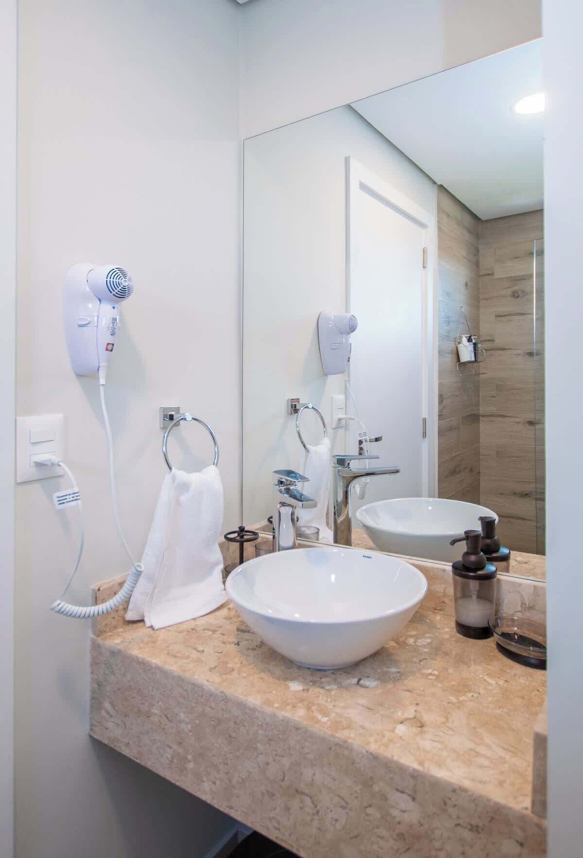 Un baño con dos lavamanos, un espejo grande y dos secadores de pelo fijos en la pared.