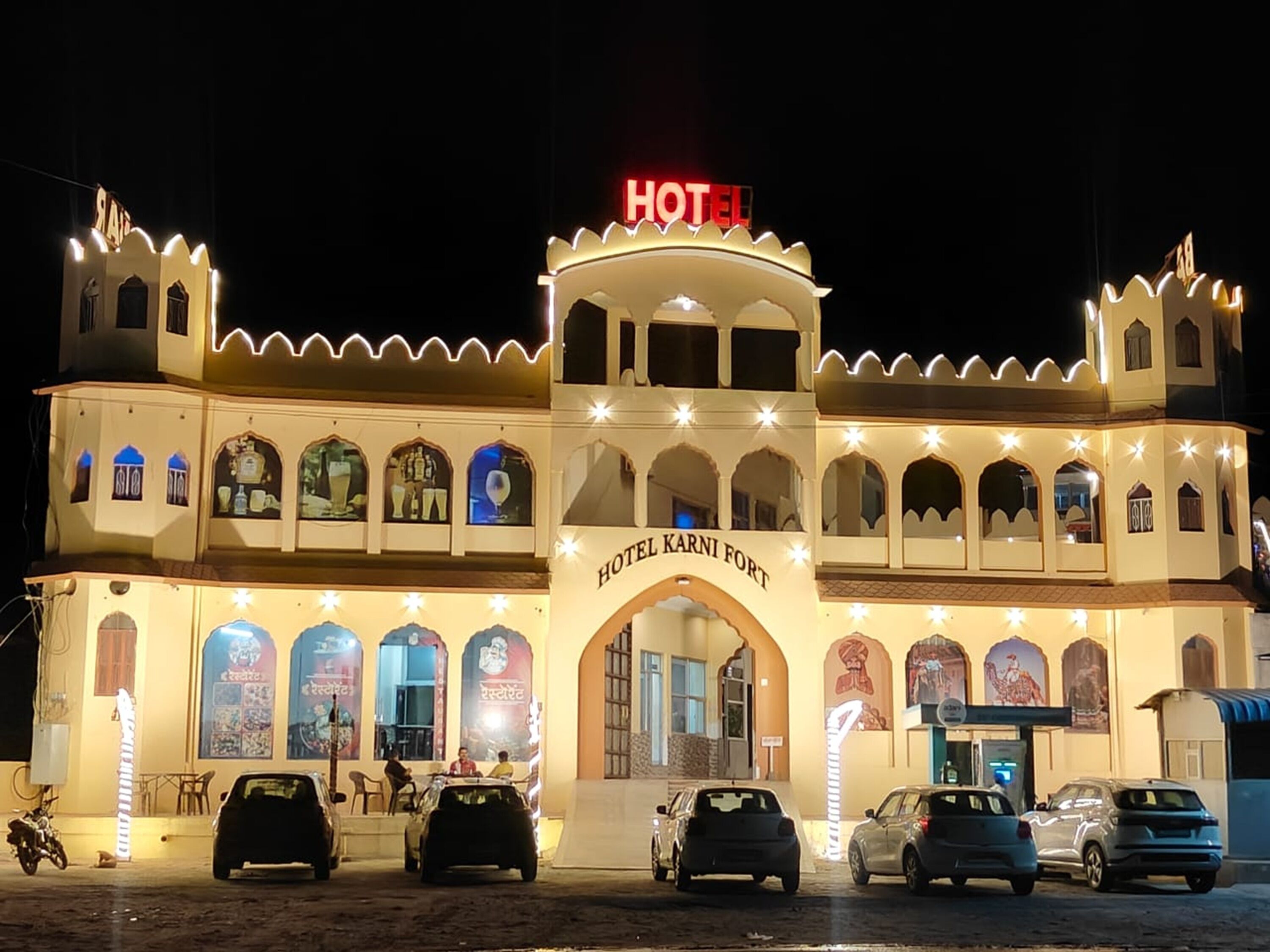 A hotel with a prominent sign reading 'HOTEL KARNI FORT' and multiple vehicles parked in front.