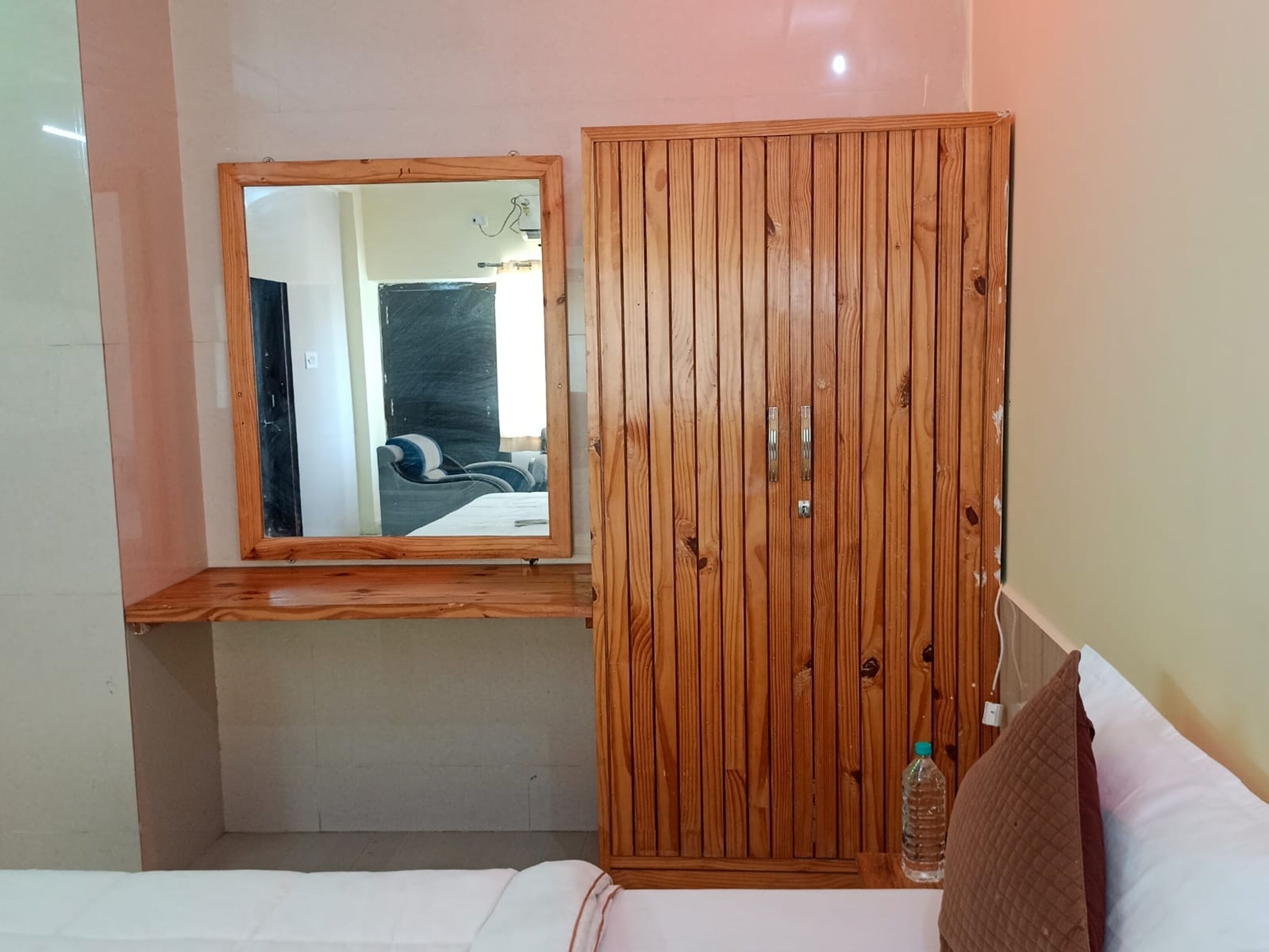 A bedroom with a wooden wardrobe, a mirror, a bed, and a bedside table.