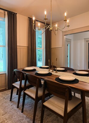 Comedor con una larga mesa de madera preparada para cuatro personas, un candelabro y vistas al exterior a través de amplios ventanales.