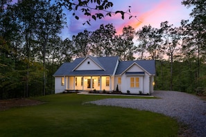 A two-story house with a front porch, surrounded by a well-maintained lawn and a gravel driveway. - Lakewood | NEW Lake Anna Luxury Retreat (Spotsylvania Courthouse)