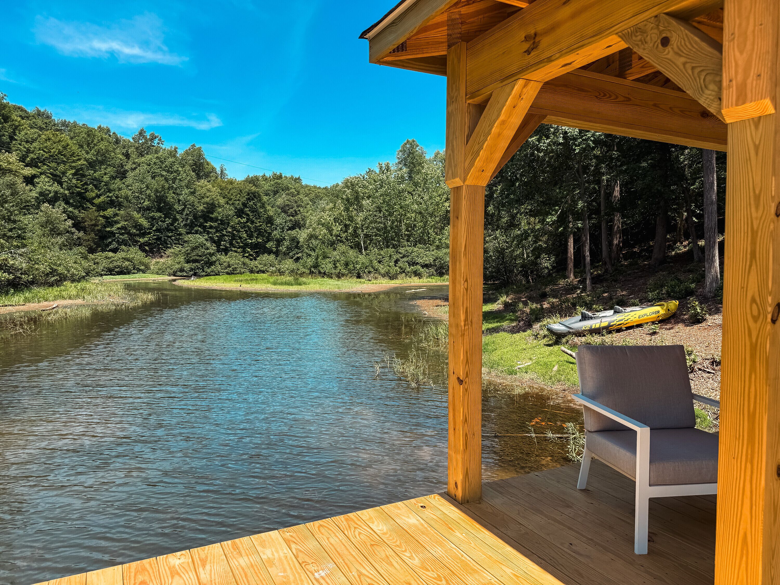 Une terrasse en bois avec un banc donnant sur une rivière paisible, le tout entouré d’une végétation luxuriante.