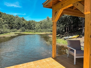 Una terraza de madera con un banco da a un río tranquilo, rodeada de abundante vegetación.