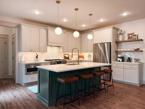 A modern kitchen with white cabinets, a stainless steel refrigerator, a central island with stools, and pendant lighting. - Lakewood | NEW Lake Anna Luxury Retreat (Spotsylvania Courthouse)