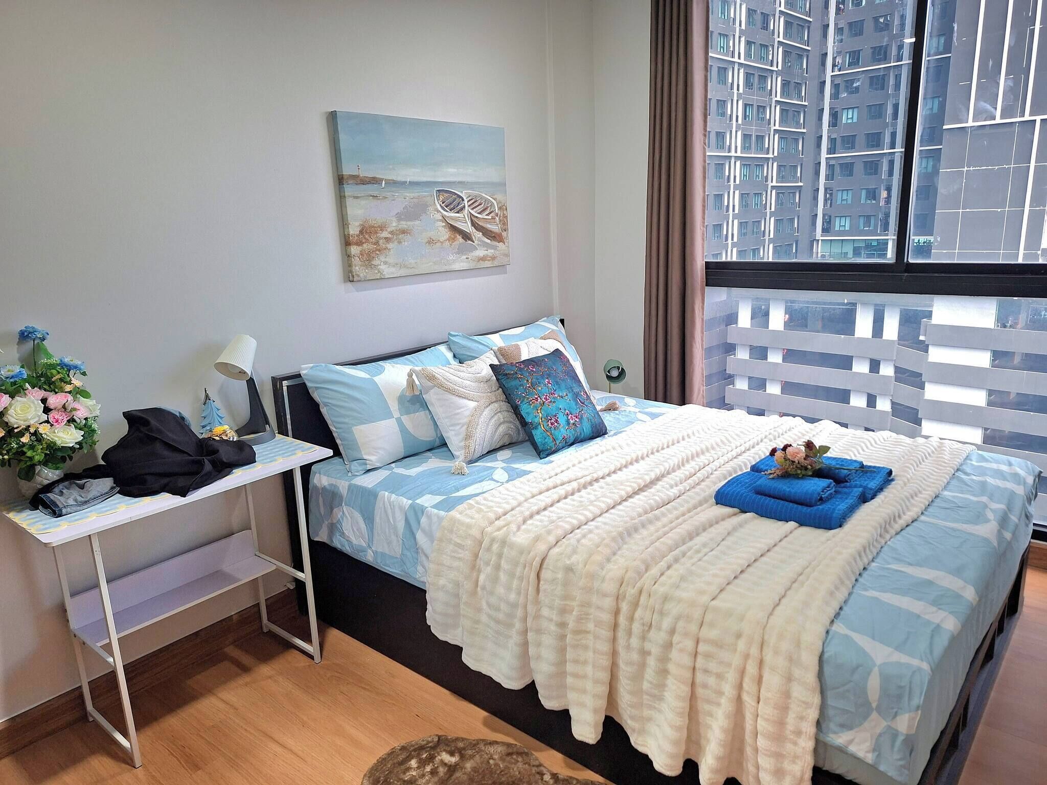 Un dormitorio con una cama, mesita de noche, lámpara y un cuadro de una playa.