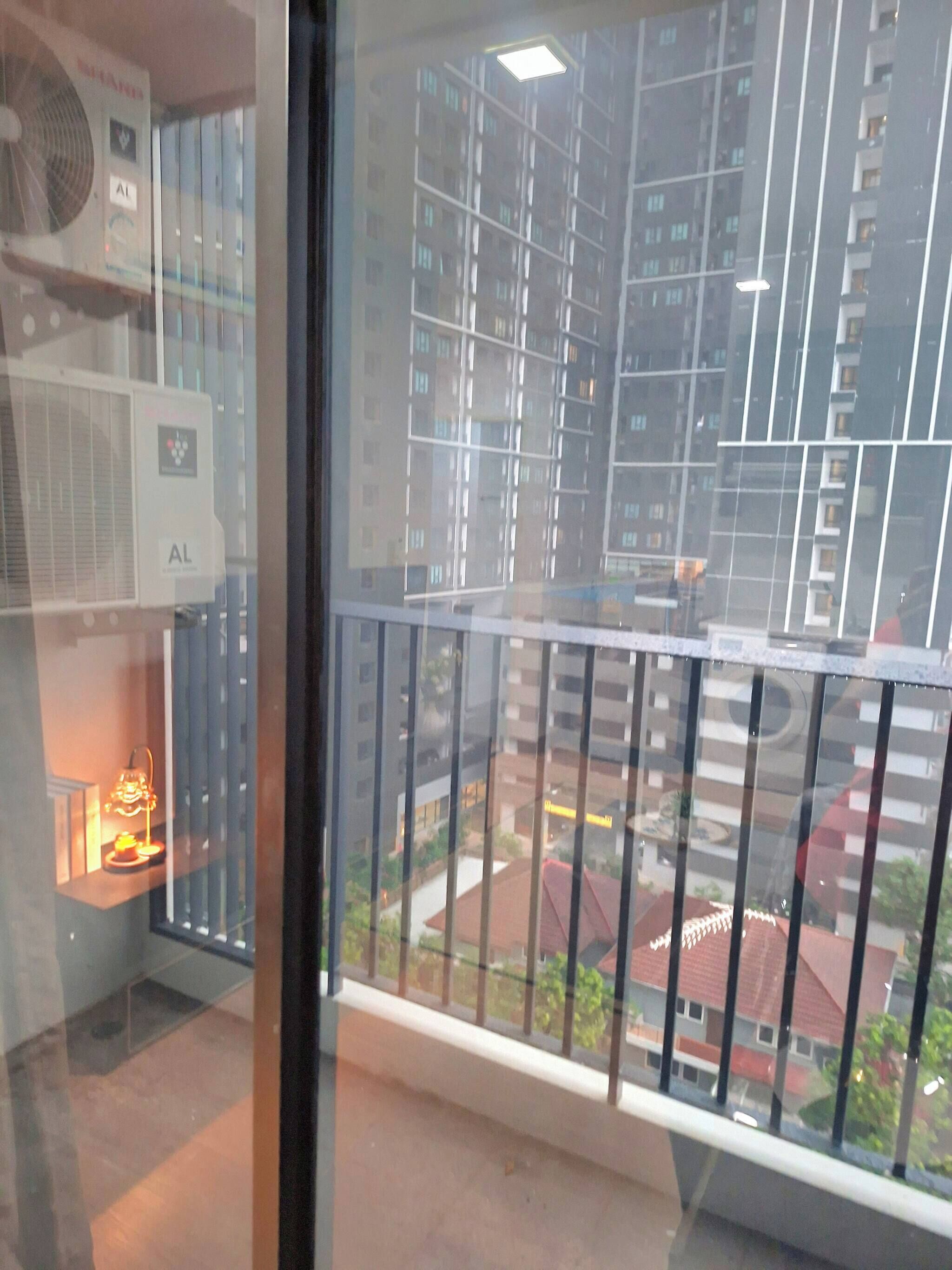 A balcony with a view of high-rise buildings, a window with blinds, and an air conditioning unit.