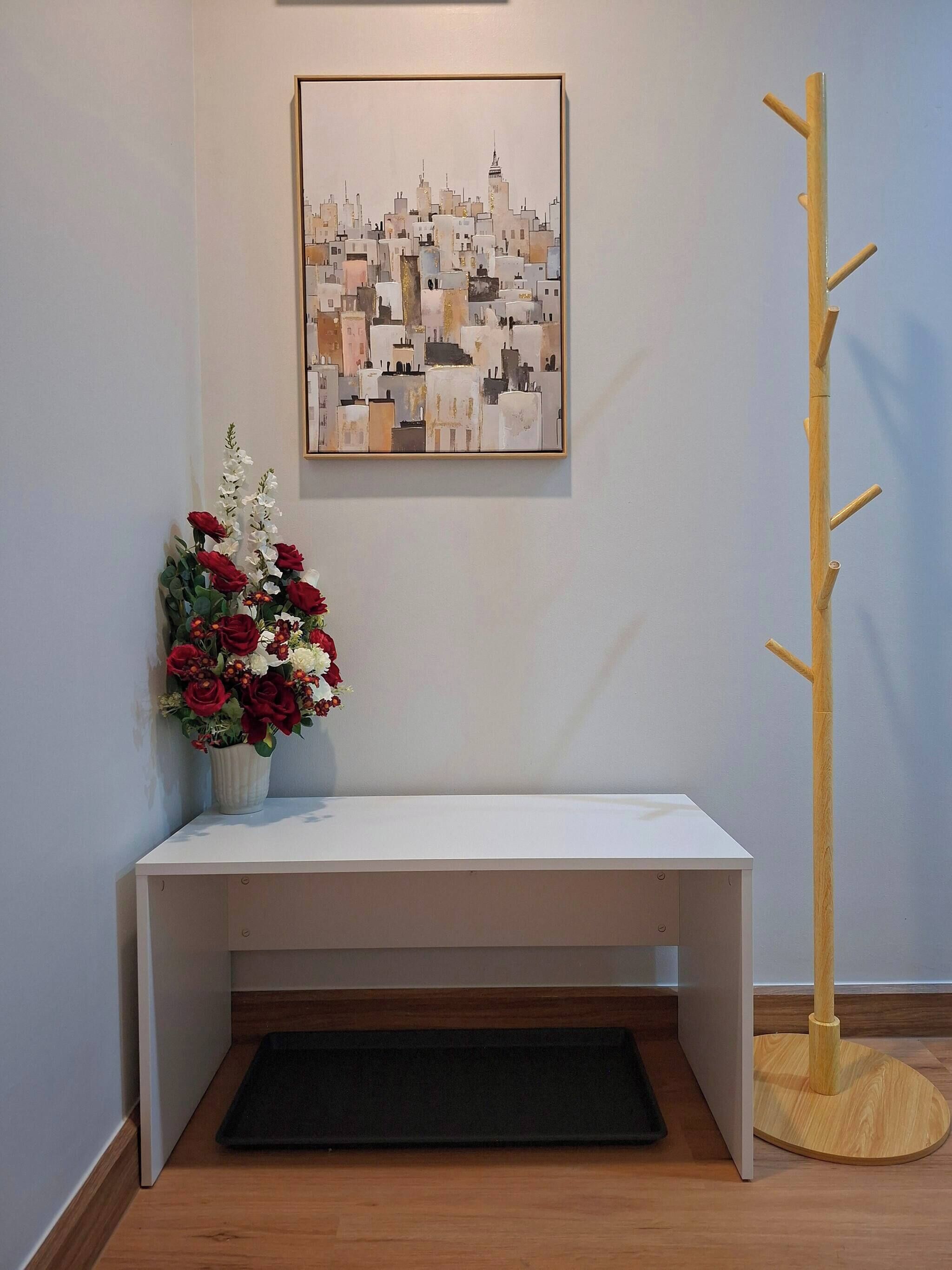 A white bench with a black mat, a wooden floor, a cityscape painting, and a wooden coat rack.