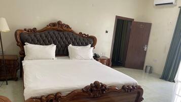 A large bed with a wooden headboard, a bedside table, a lamp, and a door in a hotel room.