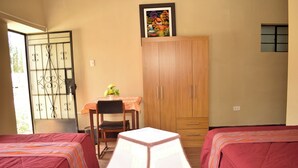 A room with two beds, a wooden cabinet, a table with a chair, and a window with a view.
