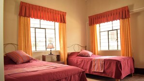 A room with two beds, a nightstand, a lamp, and a window with curtains.