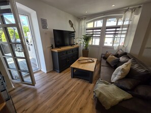 A living room with a wooden coffee table, a black sofa, a television, and a potted plant.