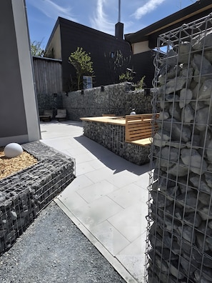 Eine Terrasse mit Steinmauer, Sitzgelegenheiten und einem Metallzaun.