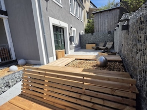 Un pati exterior modern amb bancs de fusta, una paret de pedra i una tanca metàl·lica.