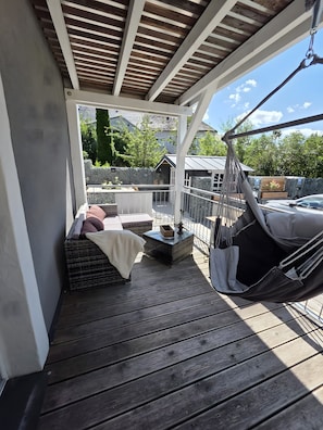 Een overdekt terras buiten, met een hangmat, zithoek en uitzicht op de omgeving.