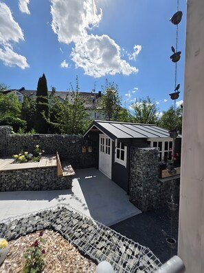 A residential backyard with a stone wall, a small shed, and a hanging bird feeder.