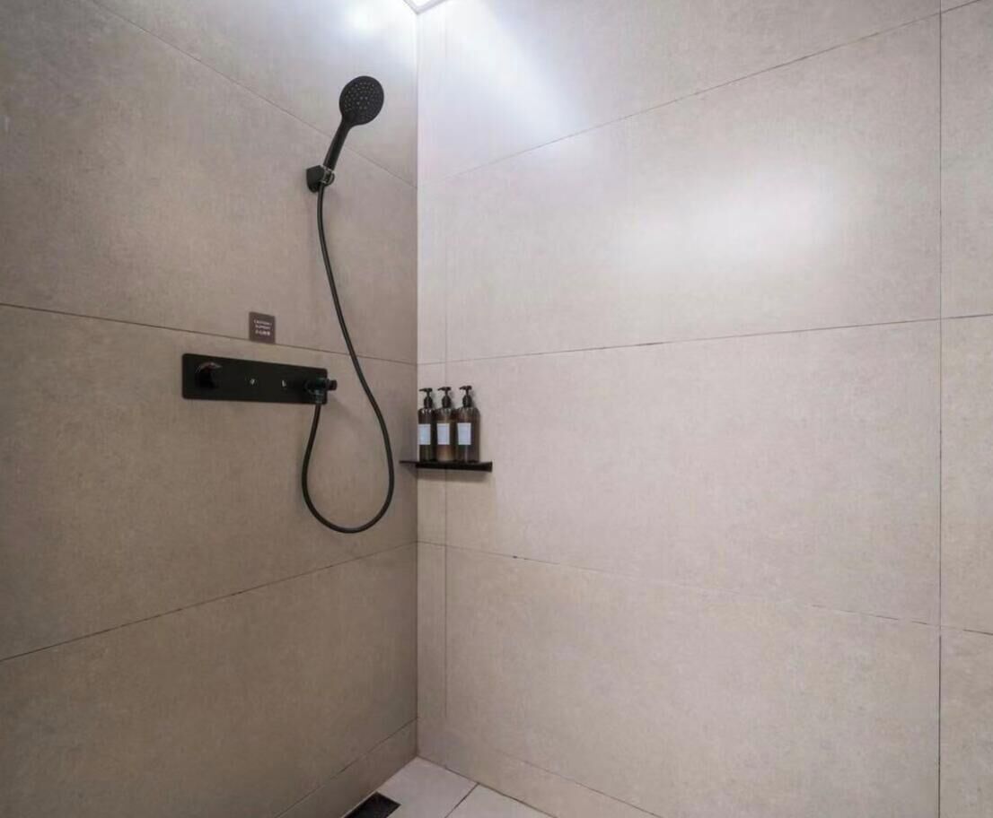 A shower with a handheld showerhead, a control panel, and a shelf with toiletries.