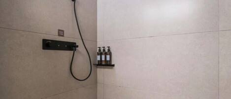 A shower with a handheld showerhead, a control panel, and a shelf with toiletries.