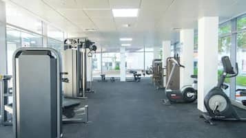 Ein Fitnessstudio mit verschiedenen Trainingsgeräten, darunter Laufband, Kraftgeräte und eine Bank.