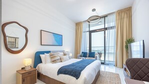Una habitación de hotel moderna con una cama grande, una mesita de noche, una silla, un televisor y un balcón con vistas.