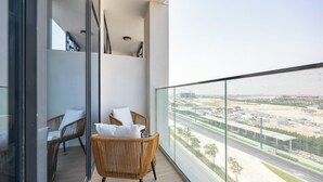 Un balcón con mobiliario de mimbre, una puerta de cristal y vistas a una autopista.