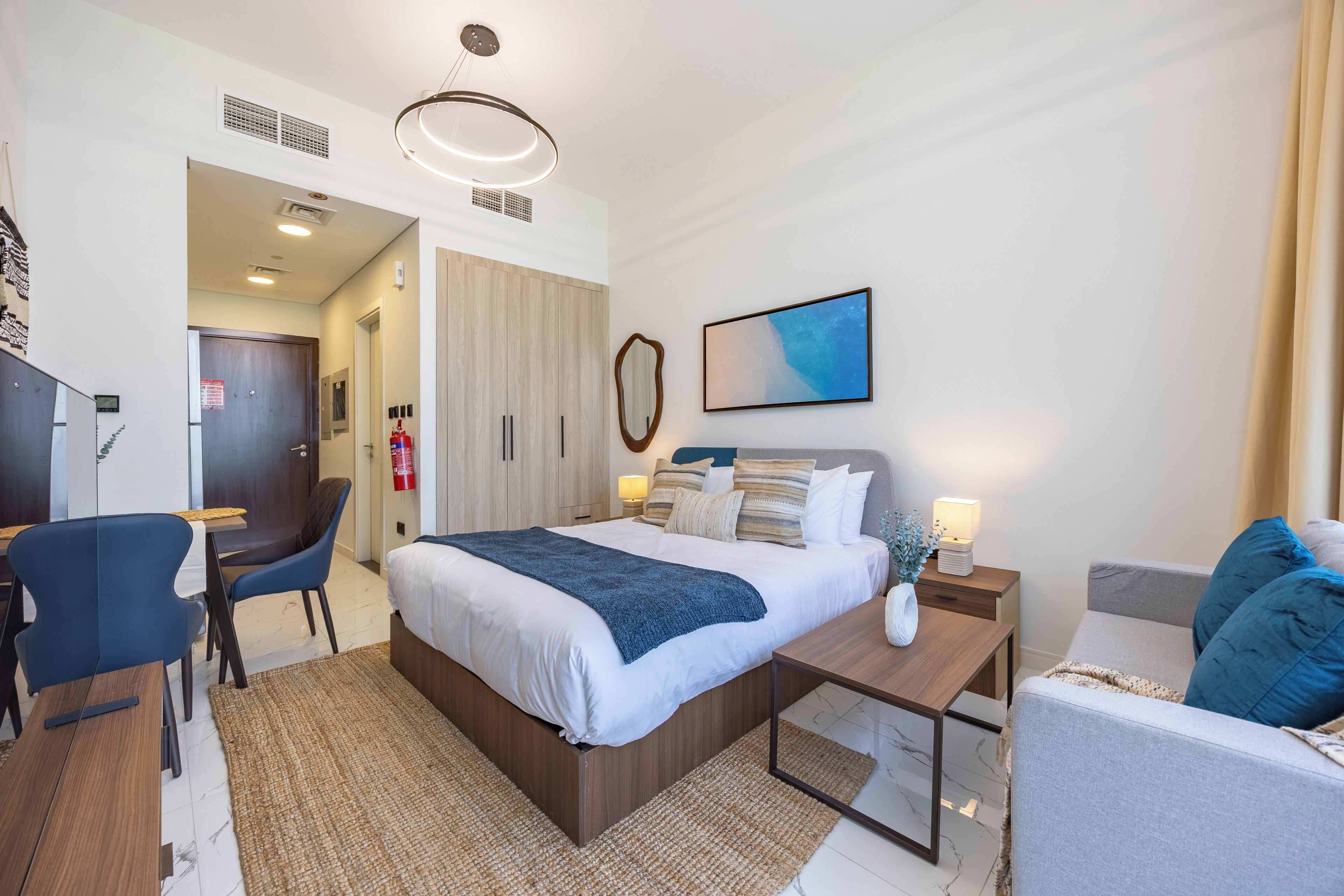 Una camera d'albergo moderna con un letto, una scrivania, una sedia e un comodino con una lampada.