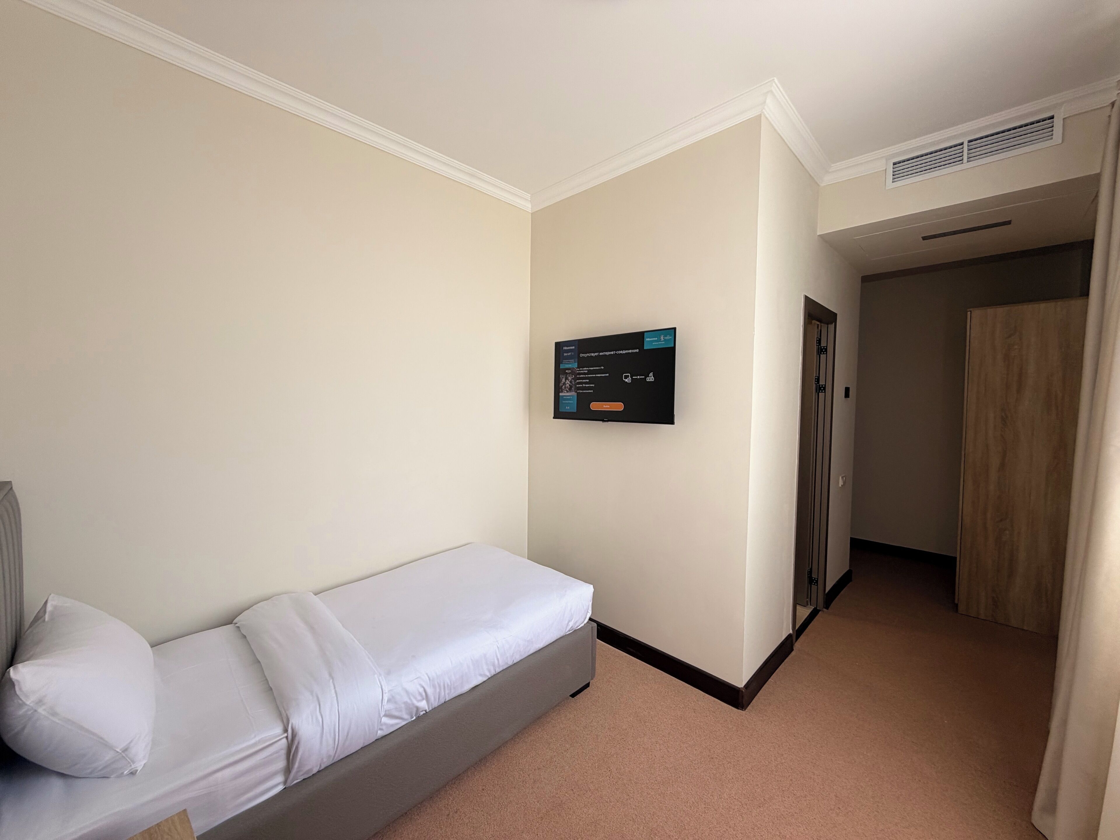 Una habitación de hotel con una cama individual, un televisor montado en la pared, una puerta y suelo alfombrado.