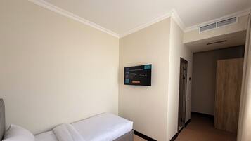 Una habitación de hotel con una cama individual, un televisor montado en la pared, una puerta y suelo alfombrado.
