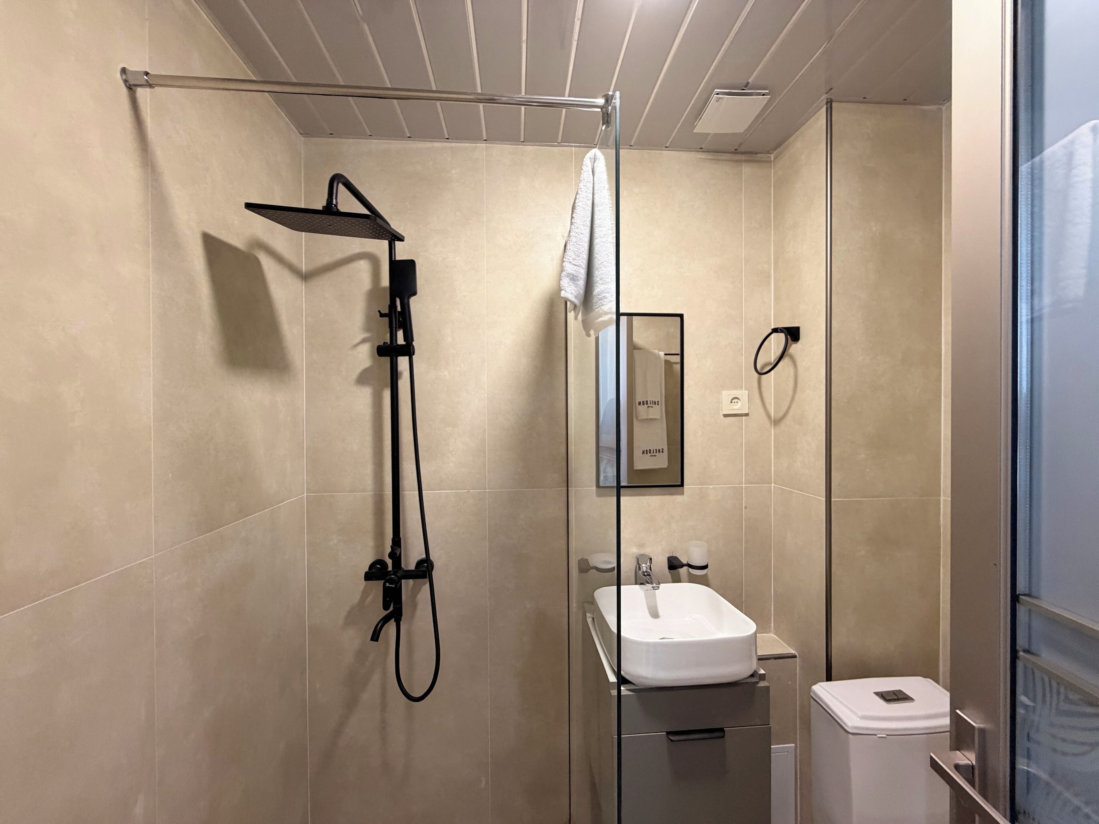 A modern bathroom with a glass-enclosed shower, a white sink, and a towel hanging on a rack.
