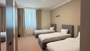 Quarto de hotel com três camas, uma janela grande com cortinas, piso coberto de carpete e uma porta.