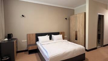 A hotel room with a large bed, a bedside table, a wardrobe, and a ceiling light.