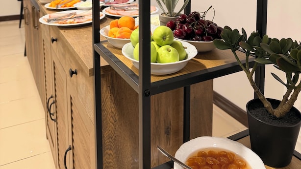 Disposição de buffet com diversas frutas, um vaso de planta e uma vitrine de vidro.