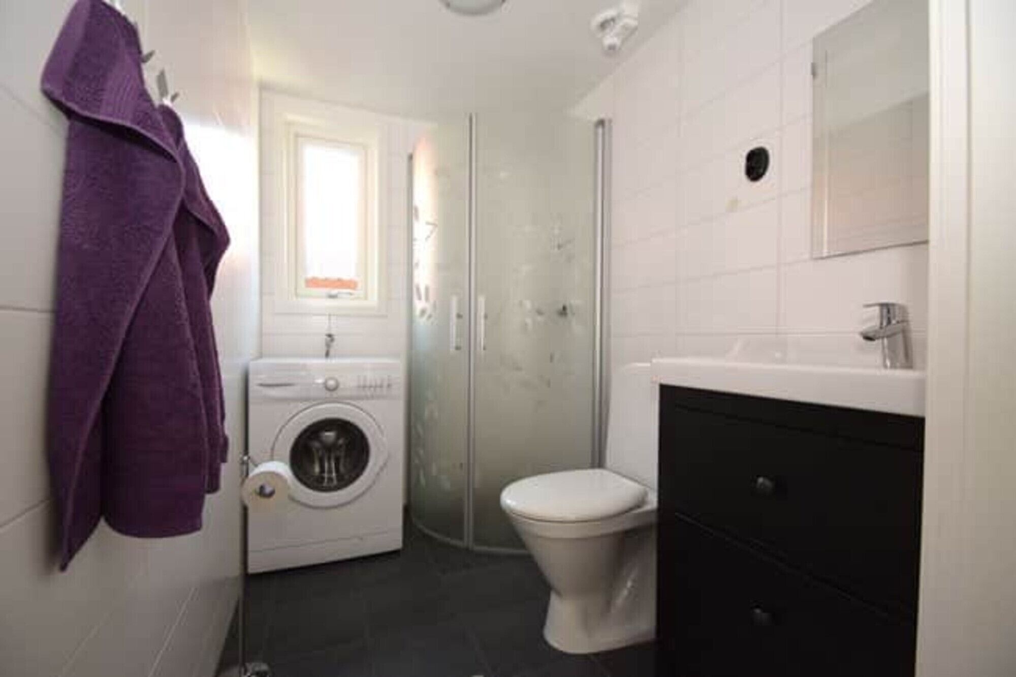 Ein kleines Badezimmer mit Waschmaschine, Toilette und einem Spiegel über dem Waschbecken.