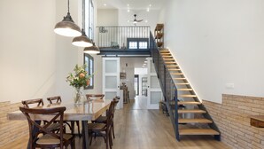 A spacious dining area with a long table and chairs, a staircase with wooden steps, and a modern kitchen in the background.