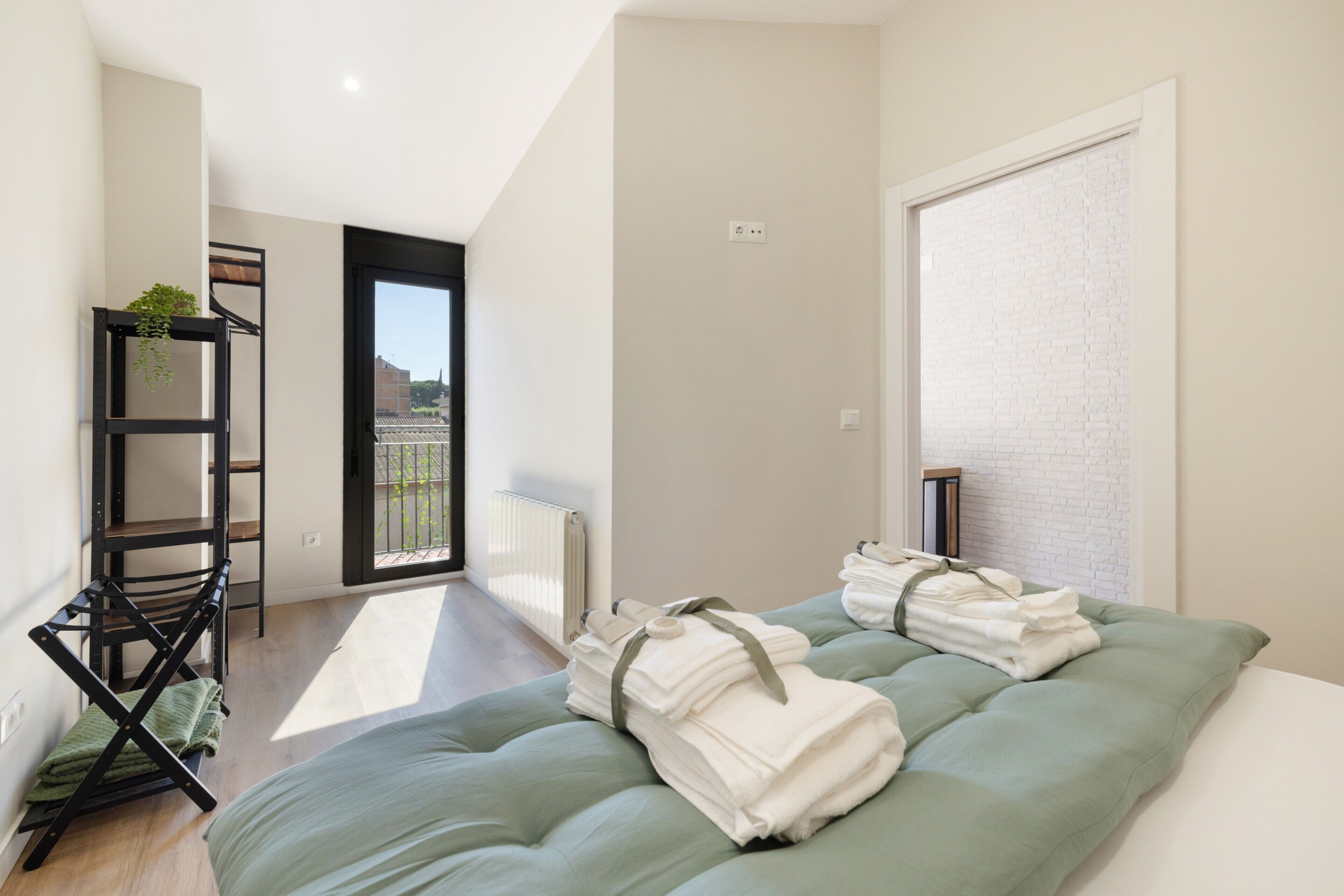 A modern hotel room with a bed, a seating area with a plant, and a view of the city.