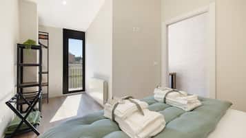A modern hotel room with a bed, a seating area with a plant, and a view of the city.