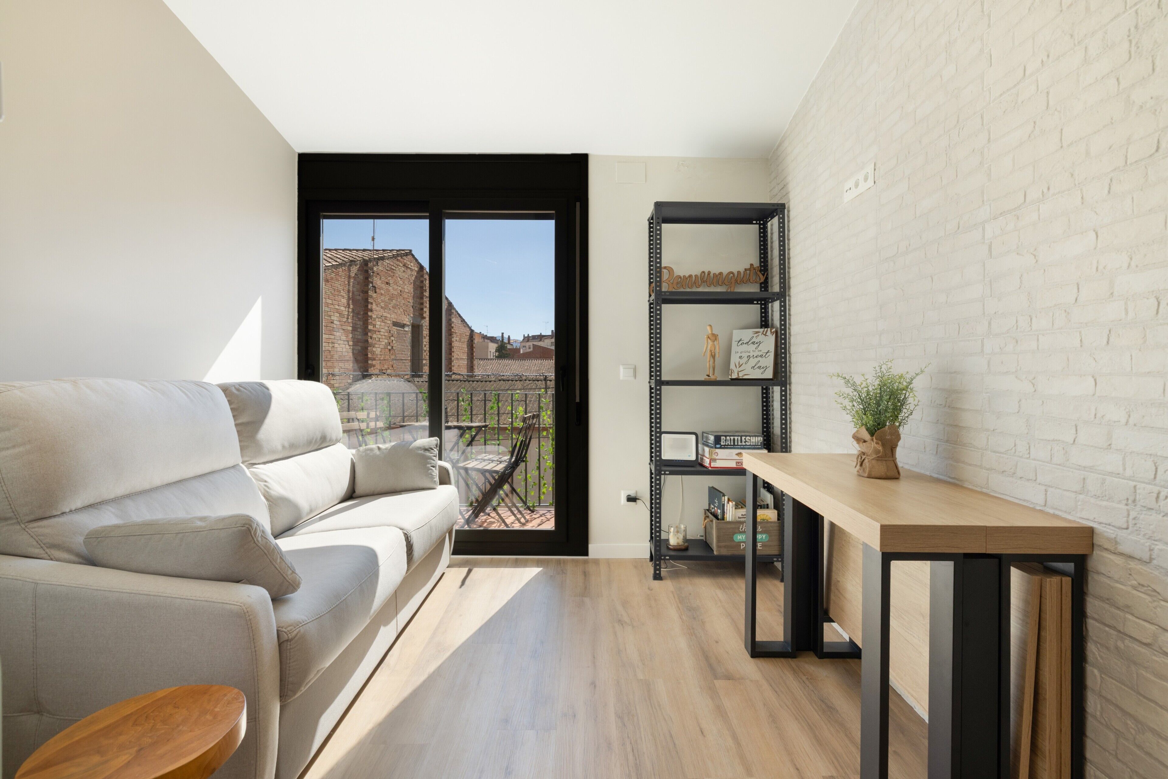 Ein modernes Wohnzimmer mit einer Couch, einem Holztisch, einem Bücherregal und einer Glasschiebetür, die auf einen Balkon führt.