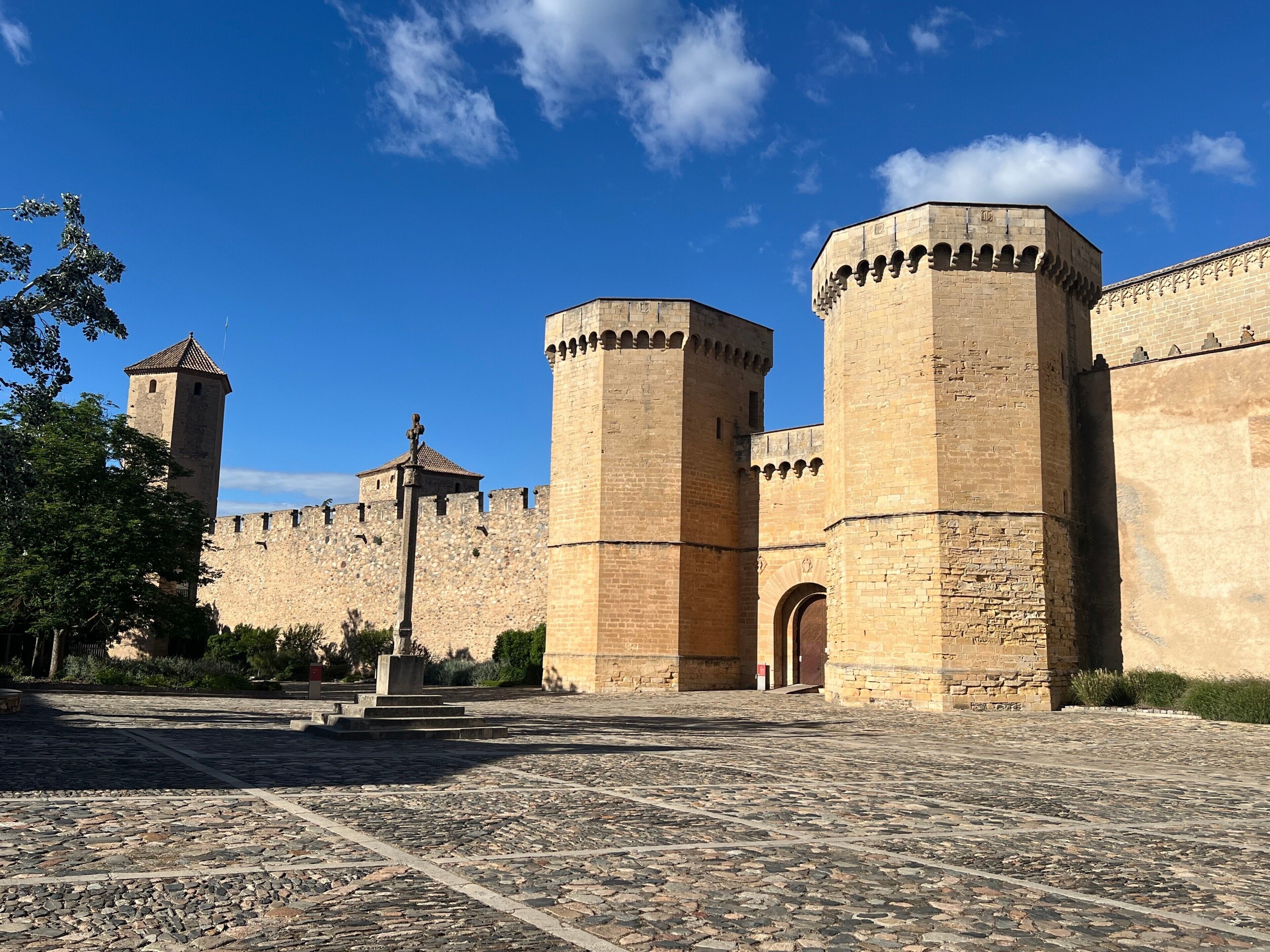 Una fortaleza de piedra histórica con una torre central, una gran entrada en arco y un patio empedrado.
