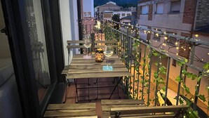 A balcony with a table set for two, a chair, and a view of the cityscape at dusk.