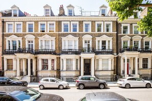 A row of terraced houses with uniform architectural style, featuring bay windows and black iron railings. - Stylish Holland Park Patio Apartment (London)