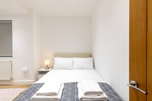 A hotel room with a bed, bedside lamp, and a door. - Stylish Holland Park Patio Apartment (London)