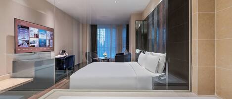 A modern hotel room with a large bed, a desk with a chair, a TV mounted on the wall, and a large window with curtains.