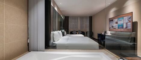 A modern hotel room with a large bathtub, a bed with white linens, a desk with a chair, and a large mirror.