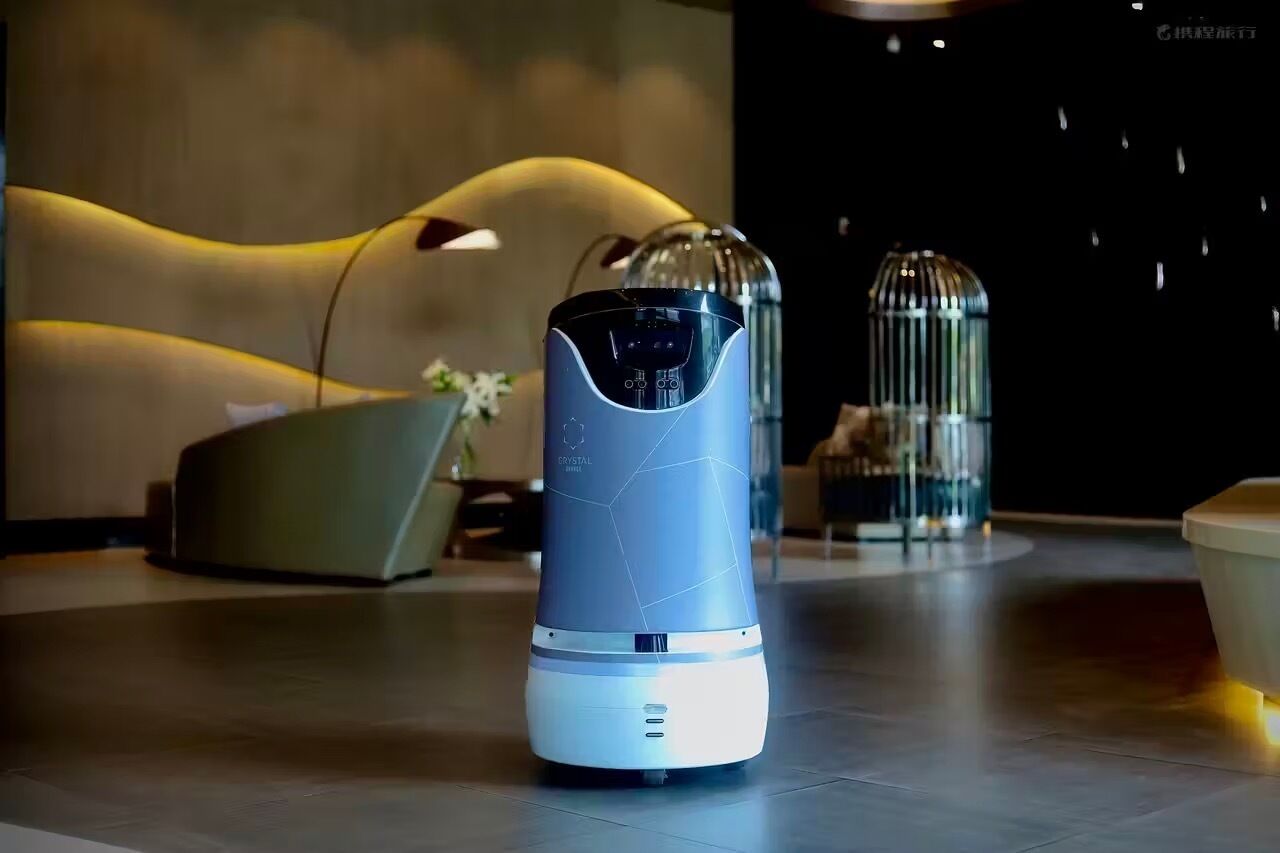Una habitación moderna y minimalista, con un dispensador de agua metálico y elegante en primer plano, un sofá con estilo y una jaula decorativa de cristal al fondo.