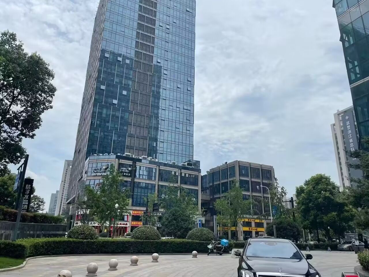 A modern high-rise building with reflective glass windows, surrounded by smaller buildings and greenery.