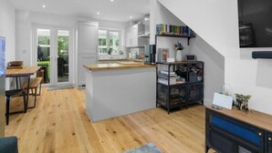 A modern kitchen with a central island, a dining area with a table and chairs, and a bookshelf with various items. - Peaceful Cambridge haven - walk to Addenbrookes (Cambridgeshire)