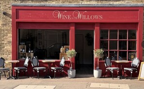 Un escaparate rojo con el nombre 'Wine at the Willows' y terraza con sillas y mesas.