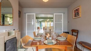 A dining area with a wooden table set for six, chairs, a fireplace, and a view into the dining room.