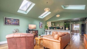 A spacious living area with a high ceiling, skylights, a sofa, a television, and a kitchen in the background.