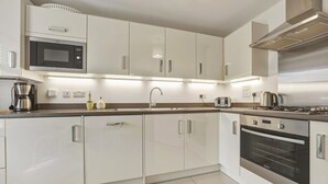 Uma cozinha moderna com armários brancos, eletrodomésticos de aço inoxidável, micro-ondas embutido e fogão a gás.
